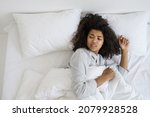 Small photo of Sleep deprivation, insomnia. Top above view of female looks over her shoulder aside, wakes up from the noise. Tired african american woman lying on uncomfortable bed in pajamas making disgruntled face