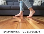 cropped shot of female legs walk barefoot on wooden warm floor near couch in living room at home, heating concept