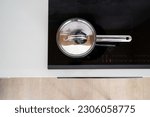 top view on stainless steel saucepan with lid on glass ceramic induction stove with temperature indicator and sensor buttons at kitchen, using modern household appliance