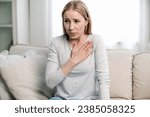 Small photo of worried woman feeling acute cardiac pain, hold hand on chest and having difficulty breathing while sitting on couch at home. young female have panic attack and afraid for her health