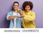 Small photo of Mixed race partners give fist bump, agree to work together, have happy facial expressions rejoice success and cooperation, have toothy smiles, isolated over purple background. Team work concept