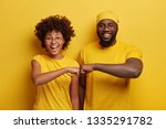 Small photo of Studio shot of overjoyed satisfied woman and man with dark skin, give fist bump, agree to work together, have success in project work, wear yellow attire, pose in studio. Cooperation concept