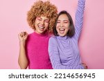 Small photo of Happy overjoyed women dance and have fun keep arms raised dressed in casual jumpers exclaim loudly apply vivid bright makeup foolish around isolated over pink background. People and fun concept