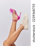 Small photo of Cropped image of unrecognizable woman wears pink high heeled shoes on one leg sneaker on other chooses between comfortable and uncomfortable footwear isolated over grey background. Elegance or sport