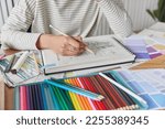 Cropped shot of unknown creative woman draws picture in album engaged in favorite activity develops her painting skills uses colorful crayons poses at table at home. Leisure pastime and hobby concept