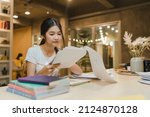 Small photo of Asian student women reading books in library at university. Young undergraduate girl do homework, read textbook, study hard for knowledge on lecture desk at college campus overtime night.