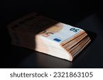 Small photo of A big wad of money half in the shade on the black table. Euro money banknotes in shadow. 50 euro pack. The concept of the shadow economy.