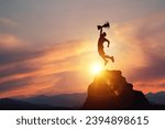 Small photo of Silhouette of a businessman jumps holding a trophy on top mountain with light sunset. concept of a successful business or determination to lead the organization to success.