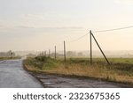 Small photo of Asphalt road among the fields and power transmission towers on a summer day after a rain - with a tamp far from the settled moisture.