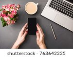 Female hands with smartphone, flowers, cup of coffee and laptop on gray table. Top view. Workplace.