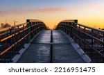 Pedestrian bridge with iron railings in the sunset sky