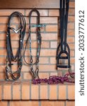 Small photo of Horse riding equipment hang on the brick wall of the stable. Halter, ropes, bit, bridle, stirrups. Equestrianism. Horse riding hobby. Background