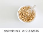Small photo of Top view of cheerios in bowl of milk with spook on right side of white table background, a healthy morning oat cereal with low sugar and high fibre for breakfast, copy space on left