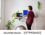 Woman telecommuting at an adjustable desk standing next to a fitball