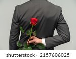 Happy valentines day. Handsome man hide rose behind back while prepare surprise for romantic date. Black suit for formal events 