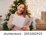 Beautiful woman laughing while reading a Christmas greeting card with light in background. Copy space for text.