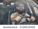 Small photo of A Young attractive man driving a vehicle, looking at scenery, seen through the windshield glass. Happy driver, holding hands on the steering wheel with a wide beautiful smile.