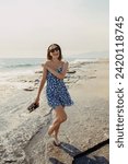 Small photo of A woman in a blue summer dress laughs heartily by the sea, embracing the carefree seaside breeze and sunshine