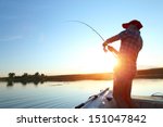 Young man fishing on a lake from the boat at sunset