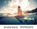 Small photo of Split shot of the young woman sitting on the surfboard in the ocean with green sunrise hills on the background