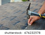 Worker hands installing bitumen roof shingles with hammer and nails.
