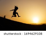 Little girl jumping over sand dunes on sunset in Maspalomas, Gran Canaria. Brave kid silhouette in the air at twilight in Canary Islands, Spain. No fear, courage, dare concepts