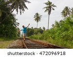 Small photo of Young man walking on railroad track while listening to music with headphones on his smartphone in rural area in Bentota, Sri Lanka. Reckless, temerarious concept