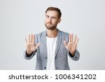 Small photo of Good-looking bearded stylish man shows palms, demonstrates absence of responsibility, isolated against gray background. Handsome young male raises hands, looks puzzled, feels guiltless. I give up!