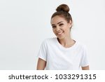 Small photo of Waist-up portrait of cheerful attractive modern woman with bun, smiling broadly at camera and expressing positive emotions wjile standing over white background. Do you want to hang around sometime