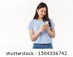Small photo of Silly asian young girl smiling brighten up day reading message from lover hold smartphone look phone screen delighted texting watching funny cute video internet stand white background