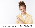 Small photo of Charming friendly helpful redhead curly messy bun hairstyle and freckles female student show way pointing left smiling pleasantly directing advertisement, giving instuctions how get place