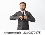 Small photo of Indecisive boss makes decision, shows thumbs up and thumbs down, like or dislike, pros and cons, looking thoughtful at camera, white background