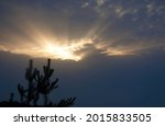 Heavy stormy dark rainy sky with cloud with sun illuminated hole over the field and forest silhouette on a summer evening, beautiful natural landscape. High quality photo