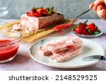 Italian strawberry dessert Semifreddo on plate with human hand holding teaspoon with strawberry's sauce