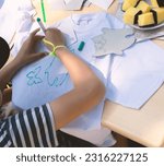 Small photo of A child uses a stencil to draw a pattern on a T-shirt.