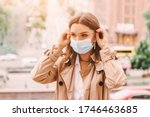 Small photo of Beautiful stylish girl wear medical face mask on sunny city street. Young elegant happy hipster woman put on protective face mask outdoors. Urban fashion outfit, lifestyle. COVID-19 quarantine, travel