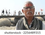 Small photo of Prayagraj,UP,01 14 2023: Portrait of a devotee having name written(Radhe) in red on forehead of his believer. A Hindu pilgrim in front of platoon bridge to river Ganges.