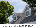 Roof shingles with garret house on top of the house among a lot of trees. dark asphalt tiles on the roof background