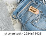Small photo of Stack of blue jeans and tag with inscription second hand. Second hand clothing shop. Circular fashion, eco friendly sustainable shopping, thrift stores concept. Top view over woman outfit