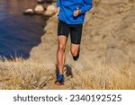 Small photo of front view runner running mountain uphill in blue jacket and black tights, trail dry grass