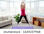 Young fitness woman doing jumping jacks or star jump exercise at home, copy space. Girl working out, full length portrait. Healthy lifestyle concept