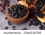 Small photo of Berries of black barberry in wooden bowl and spoon. Spice barberry blue. Dry berries of barberries.