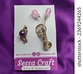 Small photo of Certainly, in a simpler manner: "Two metallic brooches, one in purple and the other in glossy metallic red, are artfully tied together with a gold ribbon. Against a clean white backdrop