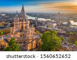 Budapest, Hungary - Beautiful golden summer sunrise with the tower of Fisherman's Bastion and green trees. Parliament of Hungary and River Danube at background. Blue sky.