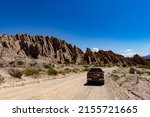 Small photo of Quebrada de las Flechas, Salta, Argentina. 02-10-2022. Dirt road with spiky mountains and red pickup seen from behind on the way to the deserted highway.