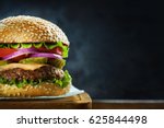 Close-up of delicious fresh home made burger with lettuce, cheese, onion and tomato on a rustic wooden plank on a dark background