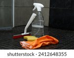 Small photo of Bathroom cleaning equipment with shower wiper, spray bottle, gloves and a sponge on grey tile floor