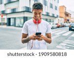 Young latin man smiling happy using smartphone and headphones at the city.