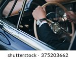 driving a retro car driver sitting in a suit and holding a steering wheel, the driver on the hand watch.