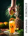 Small photo of Summer cocktail with vodka, pineapple juice, mango, ice. Long drink or cold mocktail. Bartender hand squeezes lime juice, frozen motion and flying drops. Tropical background with palm leaves